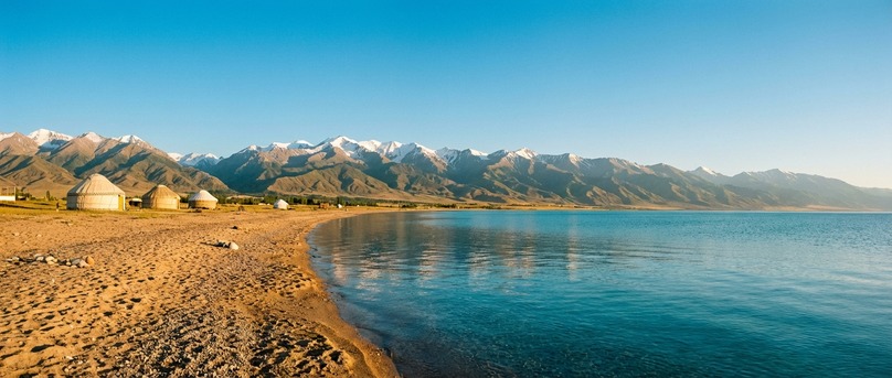 Qirg'iziston: quyoshli kunda tog' manzarasi va shahar infratuzilmasi.